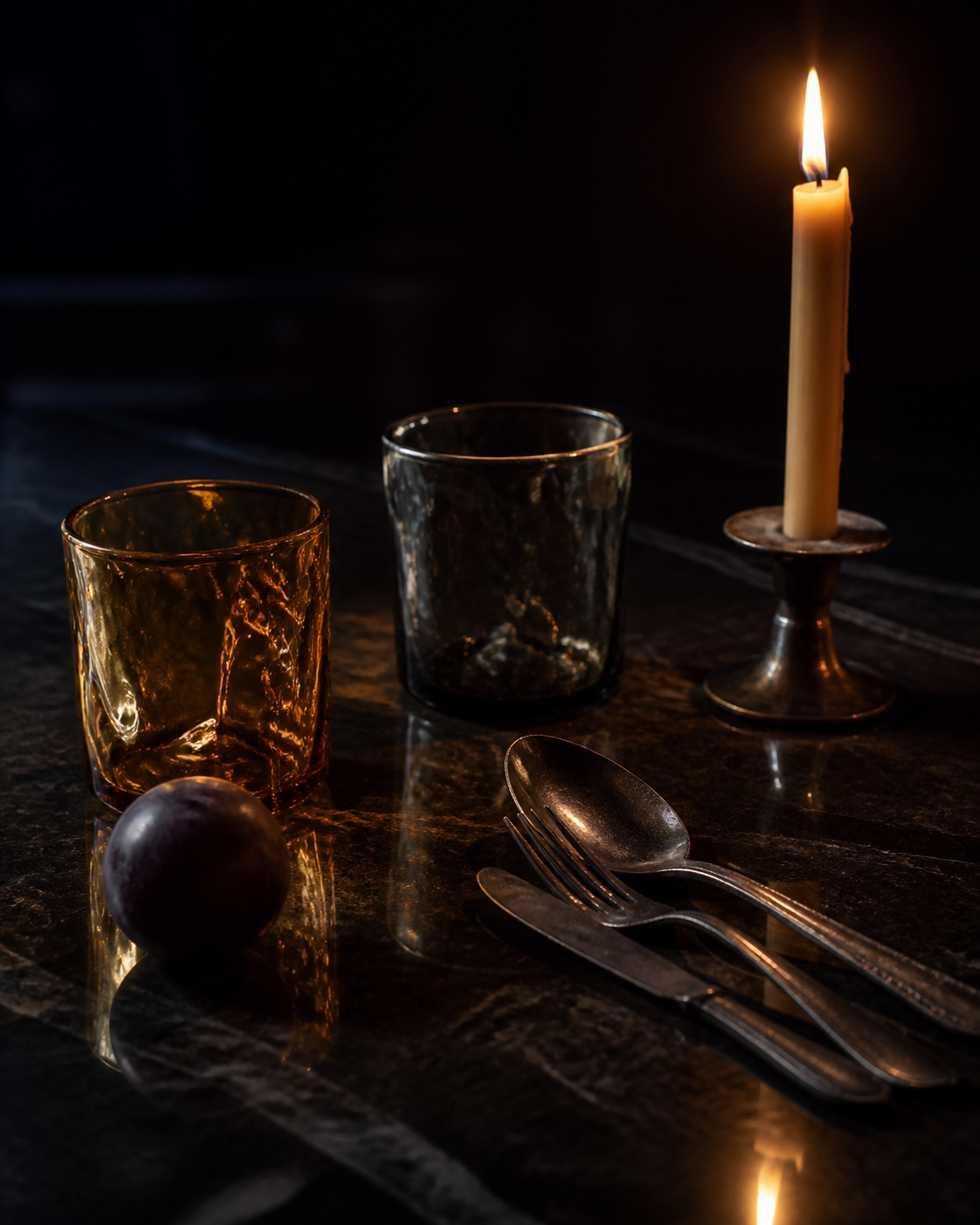 Handblown amber glass and a taper candle on a dark table